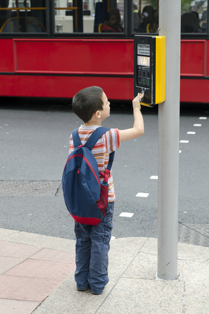 A child boy standing on a pavement or a side walk pushing the button on the traffic  signals for pedestrian crossing, road safety concept.の写真素材