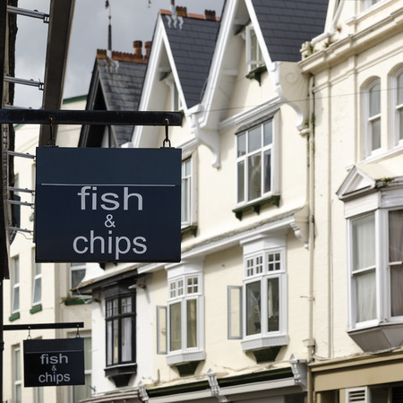 Fish and chips shop sign on a building at street of houses in England.の写真素材