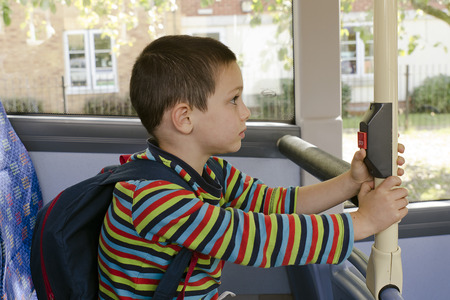 Child with school bag on a public transport city bus pressing the stop button.の写真素材