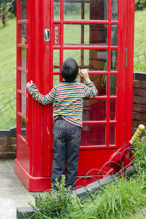 Curious child peeking in a red telephone boxの写真素材