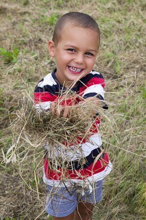 Portrait of a happy smiling child boy holding and armful of dry hay or straw.の写真素材