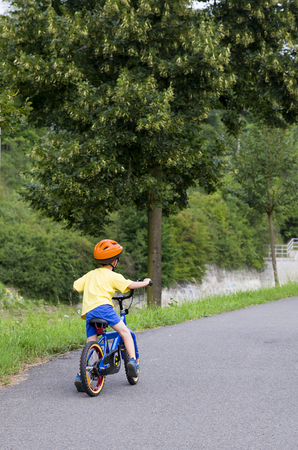 Child cycling on a cycle path along a river in summer, back view.の写真素材