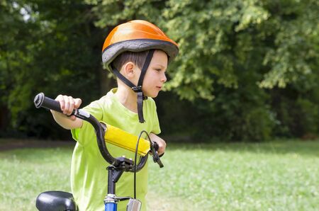 Child cyclist, potrait of a boy pushing his bicycle in a green park.の写真素材