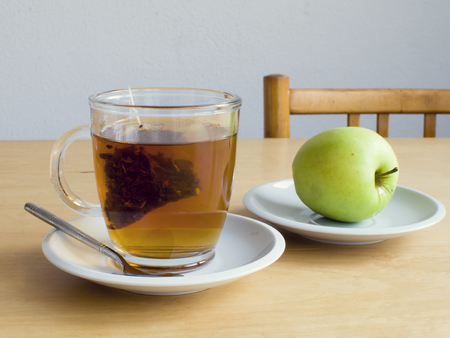 Cup of tea with teabag and a green apple on a plate on table, snack time.の写真素材