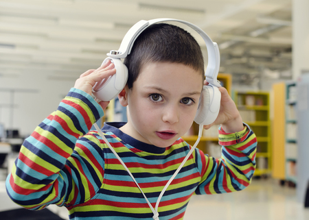 Child boy with headphones listening music or audio in a classroom or library roomの写真素材