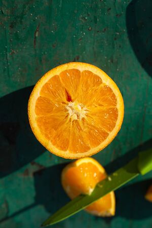slice of orange on green table, orange on green background, knife in a piece of orange on a photo, knife cuts a citrus, green knife in orange slice on green board, slicing an citrusの写真素材