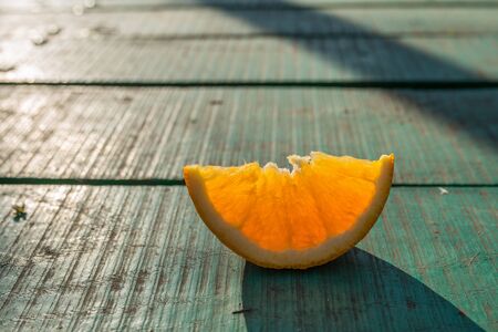 slice of orange on green table, piece of orange on green background, a slice of orange shines through the sun, the orange slice is illuminated by the sun's raysの写真素材
