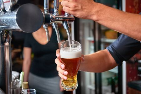 Bartender pouring beer from tap behind bar. Blurred woman in the background. Copy spaceの写真素材