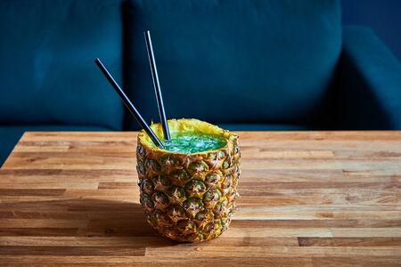 Tropical drink with ice in pineapple on the wooden table in a pub. Copy spaceの写真素材
