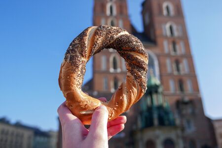 Holding bagel / obwarzanek, traditional polish snack on the Mariacka Tower background.の写真素材