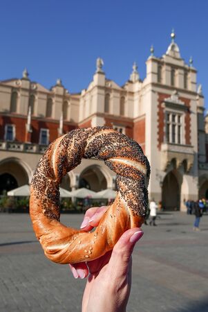 Woman holding bagel / obwarzanek / pretzel - traditional Polish snack on Market Square in Cracow. 
Tourist hand holding pretzel on the Cracow Cloth Hall background.の写真素材
