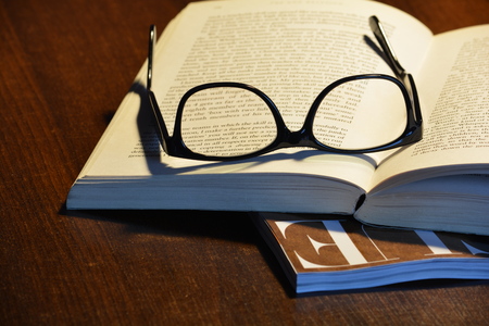 Reading glasses on an open book, and fashion mag showing underneath
