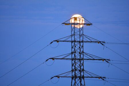 Power line pylon with a full moon in the backgroundの写真素材