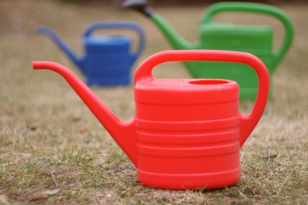 red green blue watering can on grassの写真素材