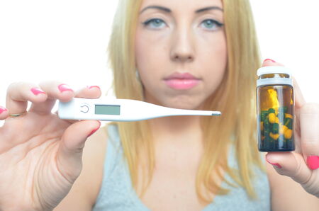 Young woman taking temperature and pills isolatedの写真素材