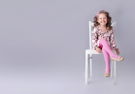 Cheerful little girl sitting on the chair with smile, a lot of copy spaceの写真素材