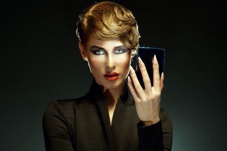 Portrait of a beautiful woman looking into mirror, isolated on dark backgroundの写真素材