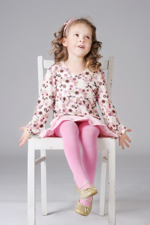 Beautiful little girl smiling, sitting on the white chair, making faces.の写真素材