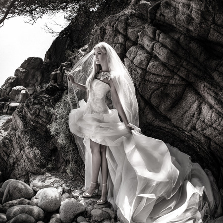 Beautiful gorgeous blonde bride posing in fashionable wedding dress outddor. Coastal view.の写真素材