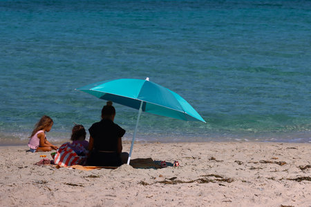 Mother and her daughter sitting on the beach under a blue umbrella.の写真素材