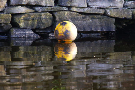Soccer ball in water with reflection of stone wall in background.の写真素材
