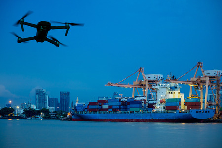 Modern RC Drone / Quadcopter with camera flying on container cargo ship at shipping port. double...