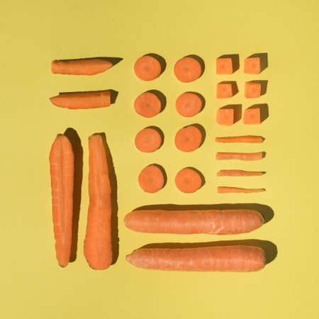 Artistic arrangement of different shapes of carrots on bright yellow background. Spring and Easter inspirationの写真素材