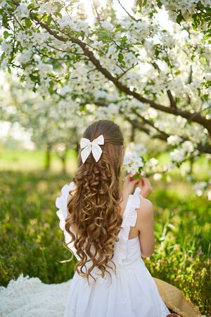 The beautiful girl the blonde in the blossoming apple-trees garden. White flowers in a garden in sunshine. Spring apple trees in blossom. Beautiful woman among spring blossomの写真素材