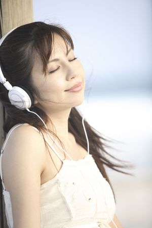 Japanese woman listening to music on a beachの写真素材