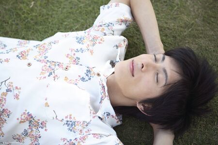 Japanese man lying down on the grassの写真素材