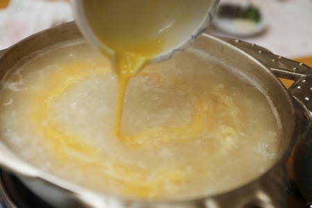 Egg is put in a porridge of rice and vegetables in pot.の写真素材