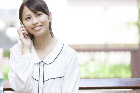 Female college students sitting to call on the benchの写真素材