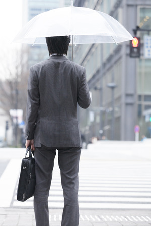 Back shot of businessman holding an umbrellaの写真素材