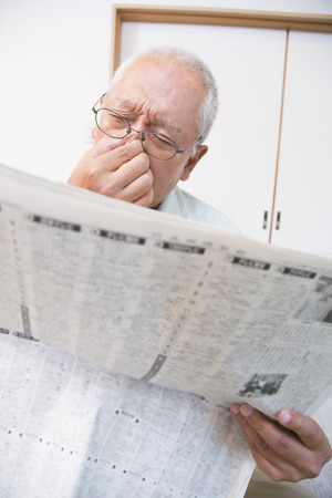 Senior man is tired eyes reading the newspaperの写真素材