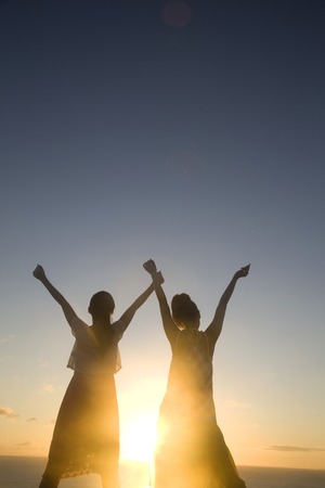 Of 2 women to spread both hands to the sky at dusk silhouetteの写真素材