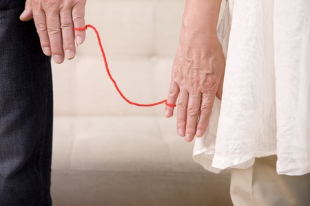 Hand of an elderly couple that was connected the little finger with a red woolの写真素材