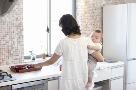Mother standing in the kitchen and holding a babyの写真素材