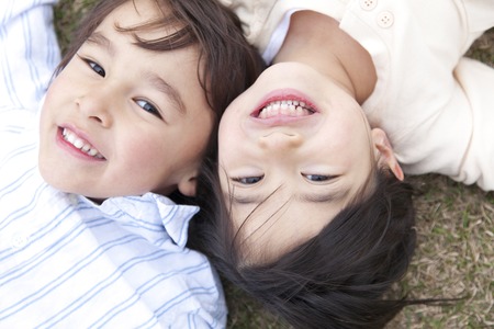 Children hand in hand, lie down on the grassの写真素材