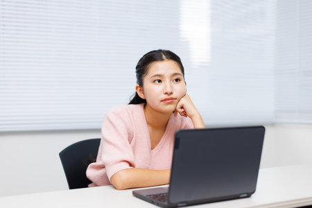 Asian teenage girl contemplating while using a laptopの写真素材