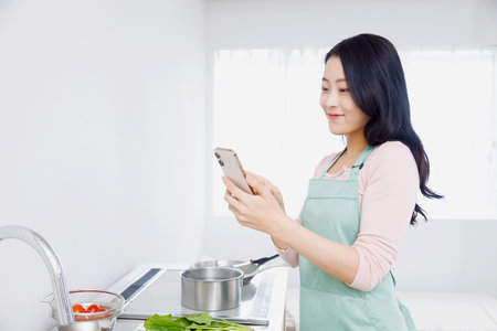 Asian woman using a mobile phone in the kitchenの写真素材