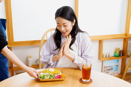 Waitress serving meal to Asian woman in a restaurantの写真素材