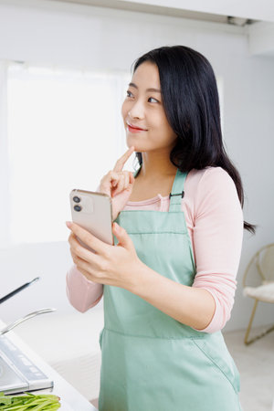 Asian woman using a mobile phone in the kitchenの写真素材