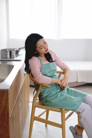 Asian woman resting on a chair in the kitchenの写真素材
