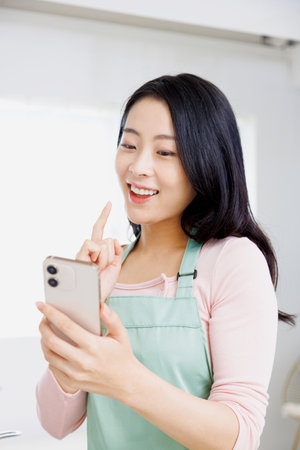 Asian woman using a mobile phone in the kitchenの写真素材