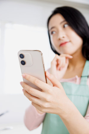 Asian woman using a mobile phone in the kitchenの写真素材