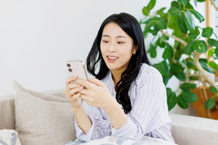Asian woman using her mobile phone in the living roomの写真素材