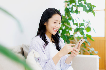 Asian woman using her mobile phone in the living roomの写真素材