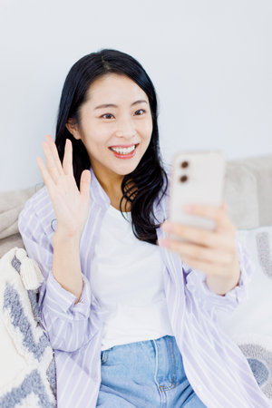 Asian woman waving to someone through video call on her phoneの写真素材
