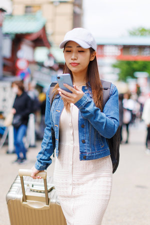 Asian woman with luggage walking in streetの写真素材