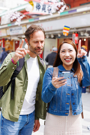 Caucasian man and Asian woman walking in street with mobile phoneの写真素材